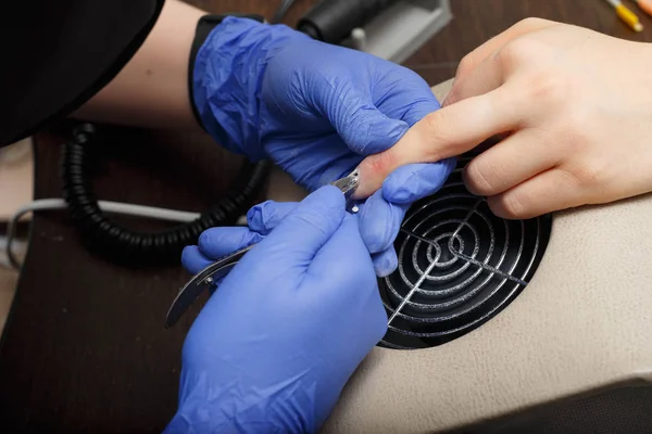 The master of nail service aligns the nails to the client with an electric machine.
