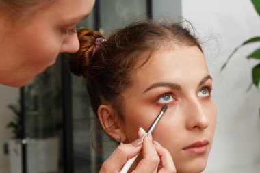 Makyaj yapma süreci. Modelin yüzünde bir fırça ile çalışan makyaj sanatçısı.