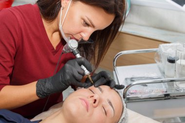 Usta, müşteriye daktiloyla kaş makyajı yapar..