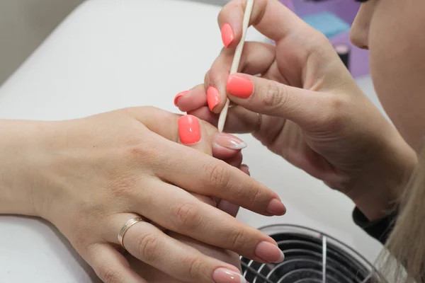 Closeup nail service mater assists cuticle removal procedure with wooden handle in salon.