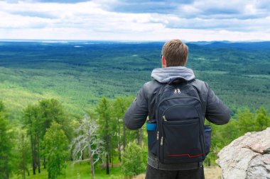 Dağlarda erkek turist. Adam bir sırt çantasıyla dağın tepesinde duruyor ve manzaranın tadını çıkarıyor. Turizm ve aktif yaşam tarzı.