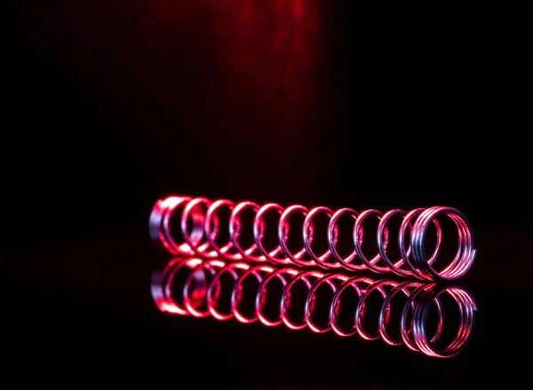 Red metal spring isolated on black background with reflection. Macro photography