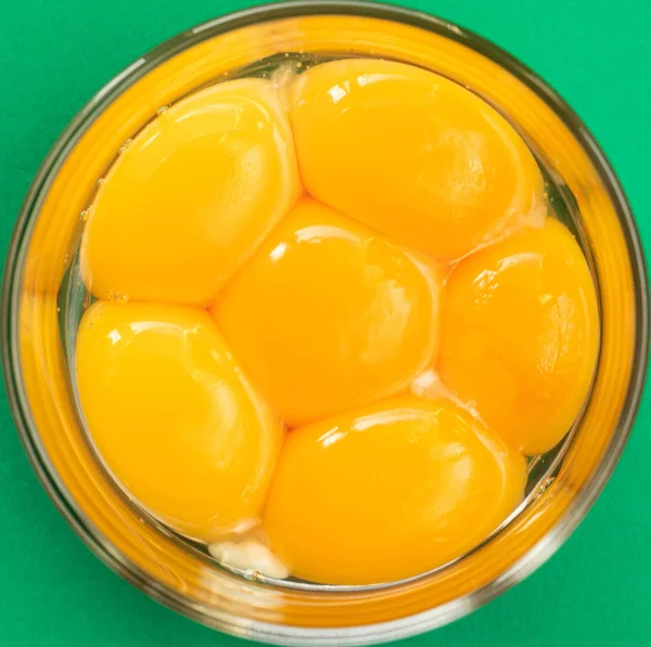 Six raw eggs in a glass bowl with beaters near yolk - Image, isolated on green background
