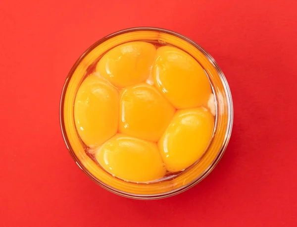 Six raw eggs in a glass bowl with beaters near yolk - Image, isolated on red background