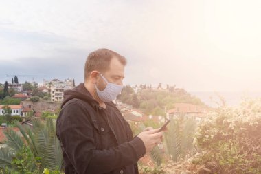 Beyaz adam dışarıda duran virüse karşı gömlek ve koruyucu maske takıyor. İnternet görüntülü mesajlar göndermek için akıllı telefon cep telefonu kullanıyor..