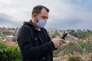 Beyaz adam dışarıda duran virüse karşı gömlek ve koruyucu maske takıyor. İnternet görüntülü mesajlar göndermek için akıllı telefon cep telefonu kullanıyor..