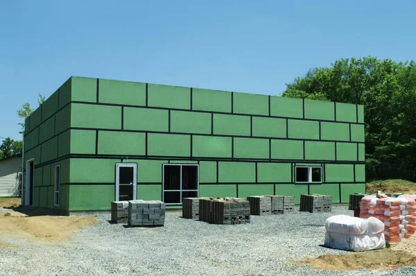 Horizontal shot of a building under construction with green insulation and the surrounding construction site.