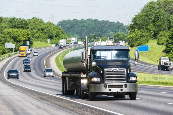 A gasoline tanker leads traffic down the interstate.  Note: All logos and identifying marks have been removed from all vehicles.  Image was created on hot day, so heat waves from the asphalt create some distortion, especially on vehicles farther from