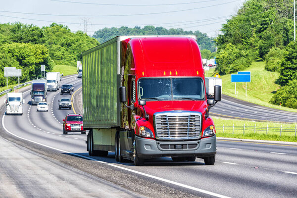 A red 18-wheeler leads other traffic down the interstate. Image shot on hot day. Heat waves from asphalt create distortion, especially on vehicles farther from camera, enhancing long telephoto effect.