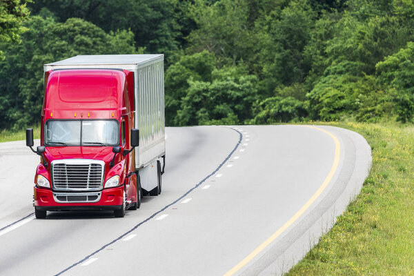A red semi crests a hill on an interstate.  The truck is placed in the image so a great deal of copyspace is created.