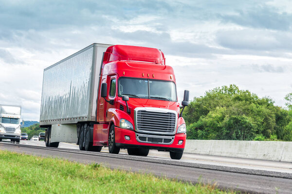Horizontal shot of a red eighteen wheeler traveling down an interstate highway