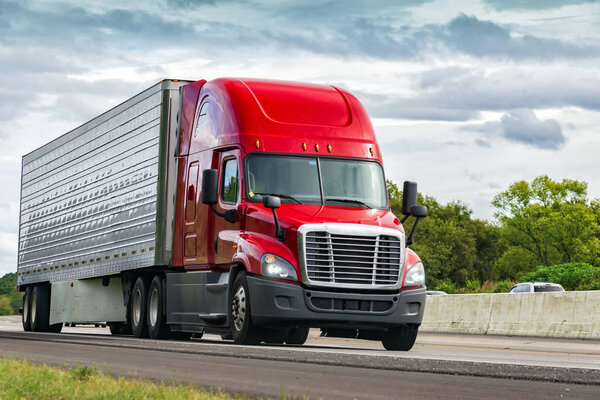 Horizontal shot of a red semi-truck on an interstate highway.
