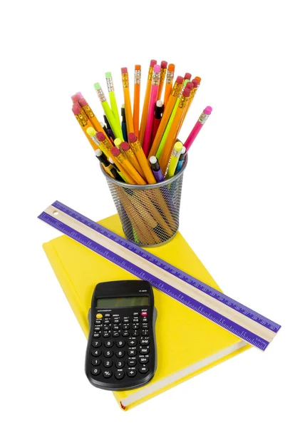 Vertical photograph of a rainbow color of pencils in pencil holder, with brightly colored yellow book, ruler and calculator. Isolated on a white background.