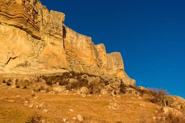 Alimova Balka Dağı, akşam güneşiyle aydınlanan parça, Bakhchisaray bölgesi, Kırım, Ukrayna. Pürüzlü dağ mavi parlak gökyüzüne karşı, ön planda kuru otlar, dağların sarı kayaları
