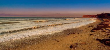 Gün batımında Cape Lucull 'un panoramik manzarası, Karadeniz, Kırım, Ukrayna. Karadeniz 'in dalgaları, sahilde yosun, burnun üstünde günbatımı, kış plajı boş.