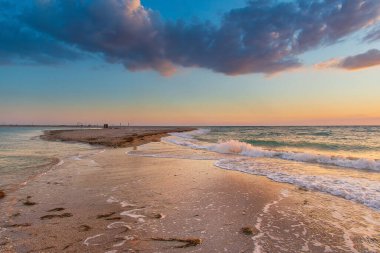 Deniz tükürüğü her iki taraftan da denizin dalgaları, gün batımı, gökyüzündeki kara bulutlar tarafından yıkanır.
