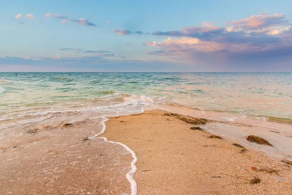 Seashore bij zonsondergang, zand wordt van twee kanten gewassen door golven, wolken in de lucht — Stockfoto