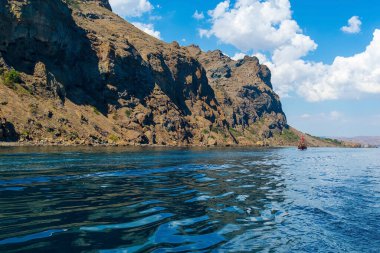Yüksek dağları olan deniz manzarası, Kırım. Mavi denizdeki dağların yansıması, uzaktaki küçük bir gemi, gökteki büyük beyaz bulutlar.