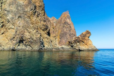 Yüksek dağları olan deniz manzarası, Kırım. Sarı dağlar ve onların yansımaları koyu mavi deniz, mavi bulutsuz gökyüzü.