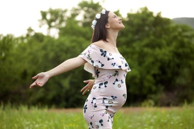 Bir çayır çiçek başında bir çelenk ile hamile mutlu kadın