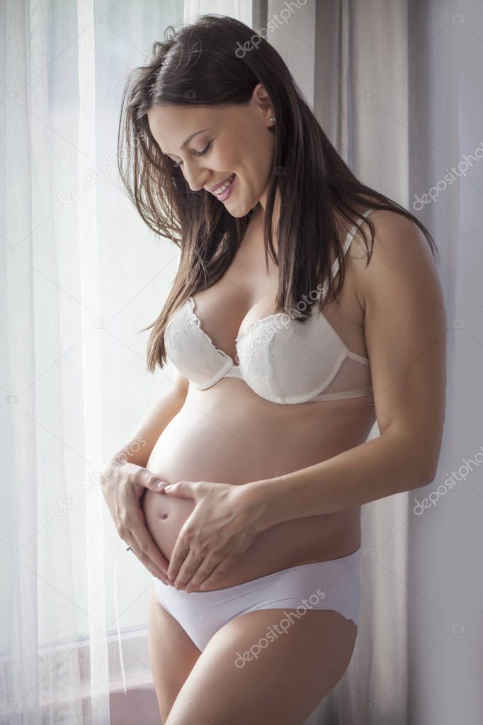 Happy pregnant woman in underwear by the window with curtains 