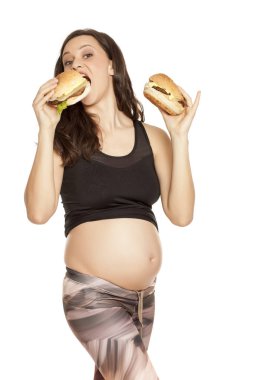 İki hamburger beyaz bir arka plan üzerinde tutan genç hamile aç gözlü kadın
