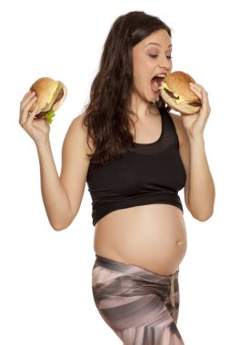 İki hamburger beyaz bir arka plan üzerinde tutan genç hamile aç gözlü kadın