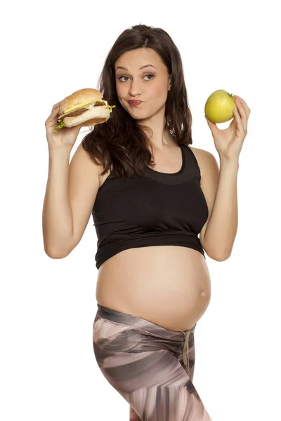 饥饿的孕妇选择在一个苹果和一个汉堡包的白色背景 — 图库照片