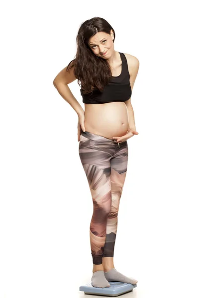 不快乐的孕妇站在一个白色背景上的体重秤 — 图库照片