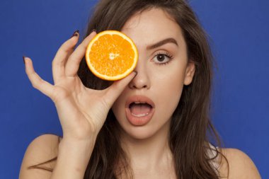 Mavi bir arka plan üzerinde yüzünde portakal dilim ile poz sürpriz genç kadın