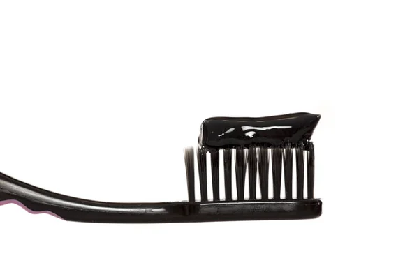 Black tooth paste with active charcoal on a black tooth brush on a white background