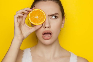 Turuncu sarı bir arka plan üzerinde yüzünde dilim ile poz sürpriz genç kadın