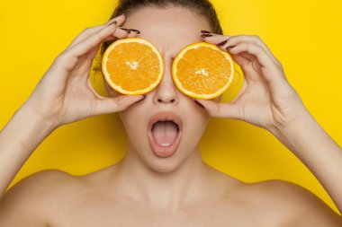 Turuncu sarı bir arka plan üzerinde yüzünde dilimleri ile poz sürpriz genç kadın