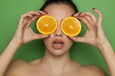 Yeşil bir arka plan üzerinde yüzünde portakal dilimleri ile poz sürpriz genç kadın