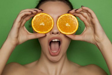 Yeşil bir arka plan üzerinde yüzünde portakal dilimleri ile poz sürpriz genç kadın