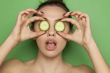 Yeşil bir arka plan üzerinde yüzünde salatalık dilimleri ile poz seksi genç kadın