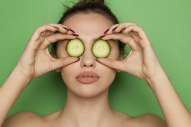 Yeşil bir arka plan üzerinde yüzünde salatalık dilimleri ile poz seksi genç kadın