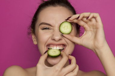 Mutlu genç kadın bir pembe bir dilim salatalık ısırma