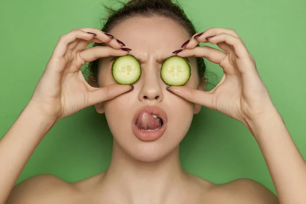 Sexy young woman posing with slices of cucumber on her face on a green background
