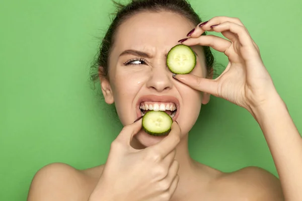 皱着眉头的年轻女子在绿色的背景下咬着黄瓜片 — 图库照片