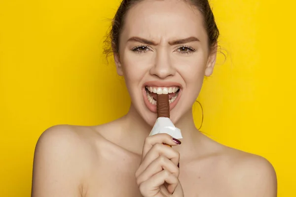 黄色の背景にチョコレートを食べることを楽しむ若いセクシーな女性 — ストック写真
