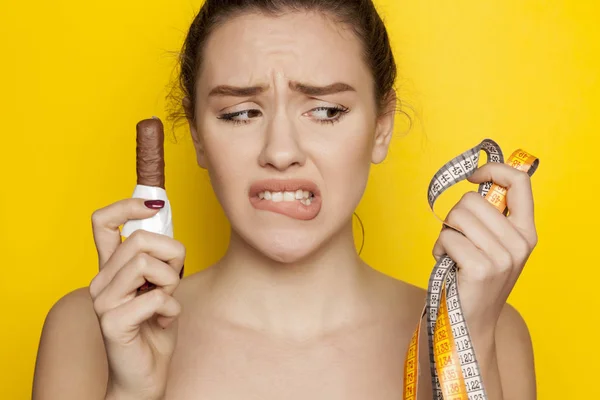 不幸な若い女性チョコレートを押し 黄色の背景に巻尺 — ストック写真
