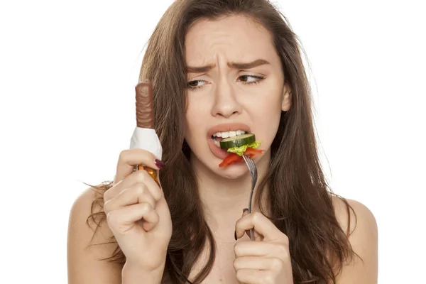 Jovem Mulher Infeliz Comendo Salada Olhando Para Chocolate Fundo Branco — Fotografia de Stock