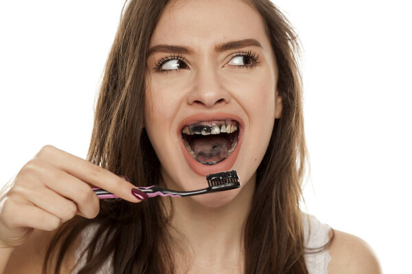 Young woman brushing her teeth with a black tooth paste with active charcoal on a white background