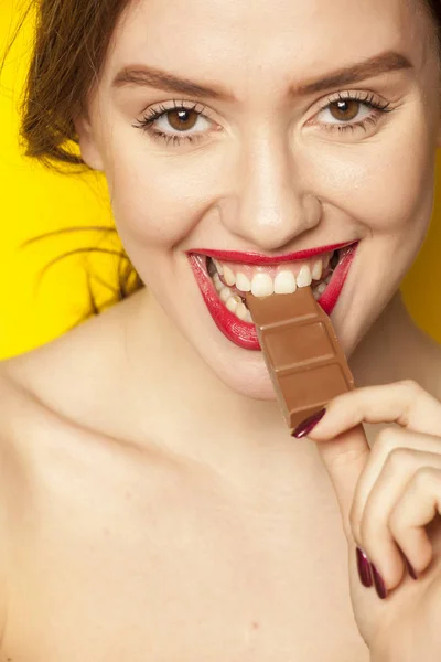 Young beautiful woman eating a chocolate on a yellow background