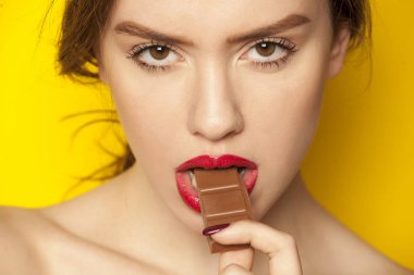 Sarı bir arka plan üzerinde bir çikolata yeme genç güzel kadın