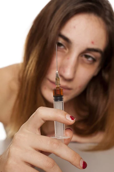 Girl with dark circles around her eyes holding a syringe. Drugs addiction concept