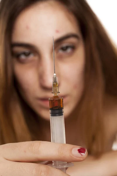 Girl with dark circles around her eyes holding a syringe. Drugs addiction concept