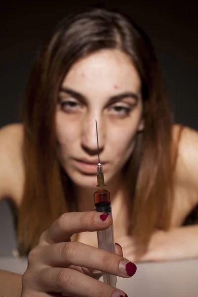 Girl with dark circles around her eyes holding a syringe. Drugs addiction concept