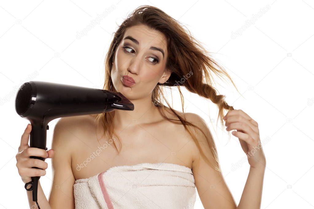 Young beautiful woman drying her hair with a blow dryer on a white background
